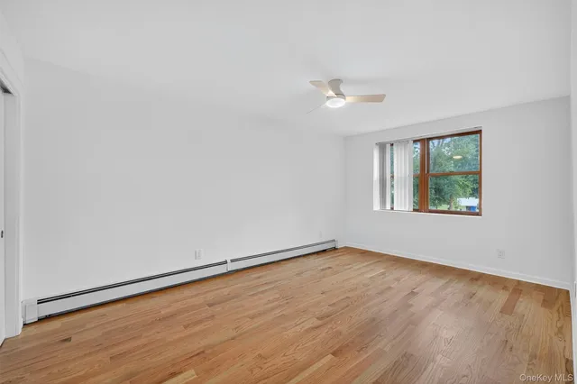 an empty room with wooden floor ceiling fan and windows