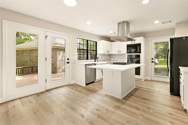 a large kitchen with stainless steel appliances granite countertop a stove top oven a refrigerator a sink and a white cabinets with wooden floor