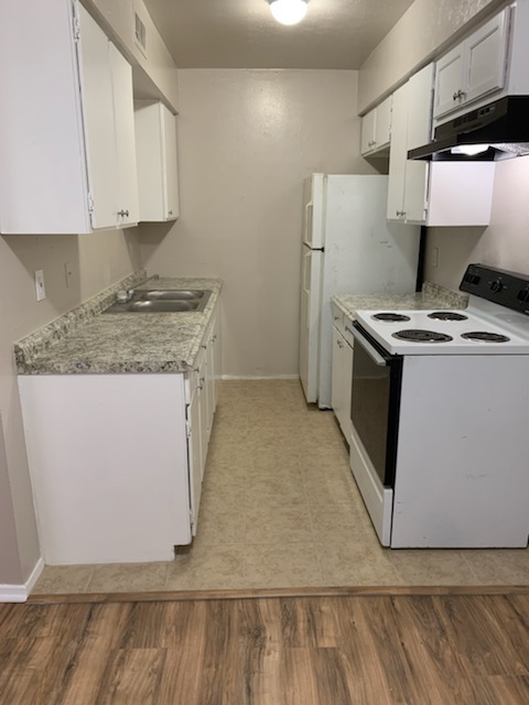 2701 Poplar Circle, Unit G Bryan, TX 77801 - Photo 3 of 8 Kitchen with white range with electric cooktop, under cabinet range hood, white cabinetry, light countertops, and light wood finished floors