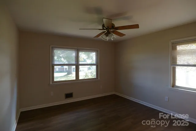 an empty room with wooden floor fan and windows