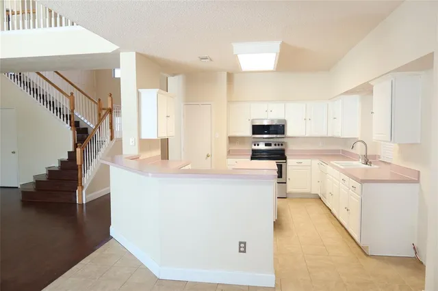 a large kitchen with stainless steel appliances granite countertop a stove top oven a sink a refrigerator and white cabinets with wooden floor