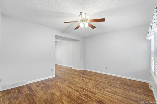 an empty room with wooden floor fan and windows
