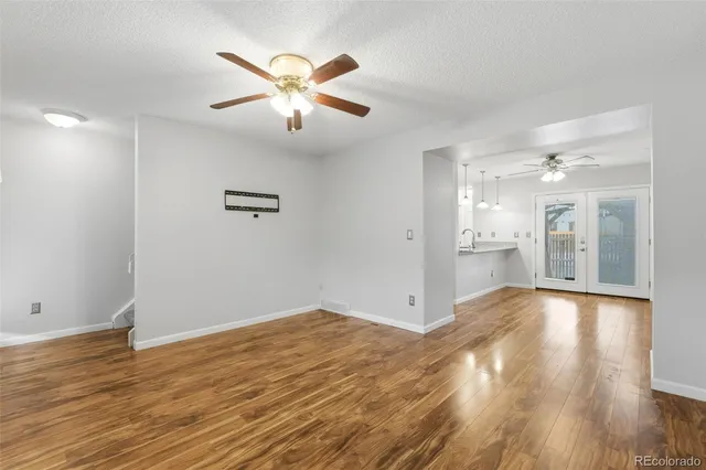 a view of an empty room with wooden floor and a ceiling fan
