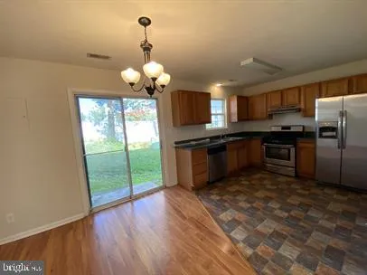 a kitchen with stainless steel appliances granite countertop a refrigerator a sink dishwasher a stove and white countertops with wooden floor