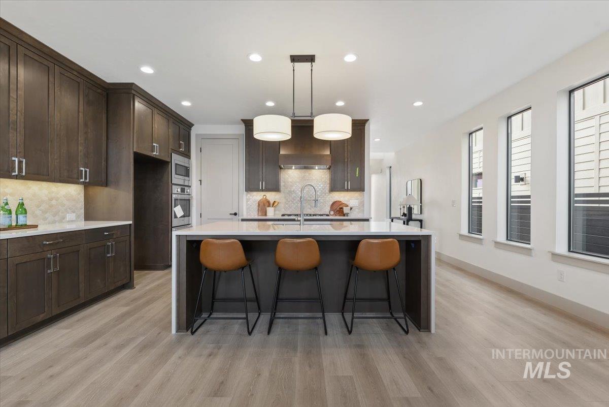 7580 West Old School Street, Unit FREMONT Meridian, ID 83646 - Photo 5 of 28 Kitchen featuring a breakfast bar area, light stone countertops, decorative light fixtures, dark wood finish cabinets, and a center island with sink
