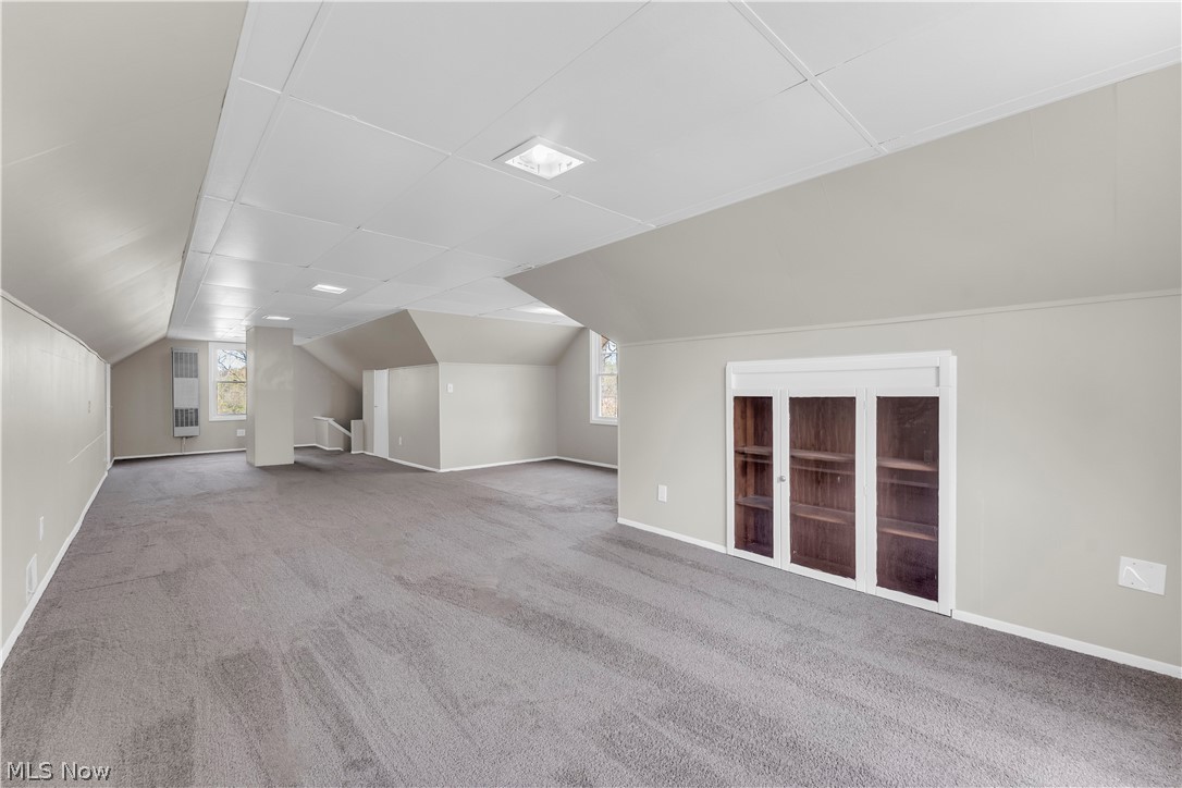 18123 McCracken Road Maple Heights, OH 44137 - Photo 18 of 27 Spacious room featuring sloped ceilings, gray carpeting, and a built-in cabinet with glass-paneled doors
