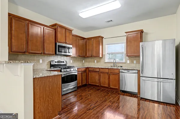 a kitchen with granite countertop wooden floors stainless steel appliances and a counter space