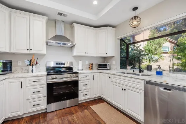 a kitchen with stainless steel appliances granite countertop a stove a sink dishwasher and white cabinets with wooden floor