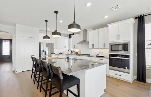 a kitchen with stainless steel appliances kitchen island granite countertop a stove a sink a microwave a refrigerator and white cabinets with wooden floor