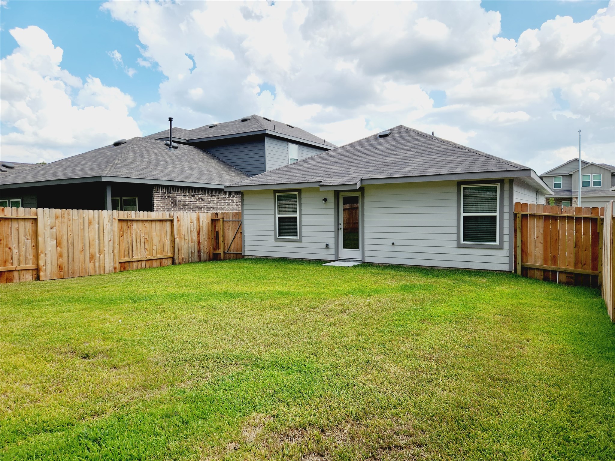 6043 Canyon Dawn Drive Spring, TX 77373 - Photo 30 of 31 A cozy backyard with a well-maintained lawn, enclosed by a wooden fence, perfect for outdoor activities and privacy. The house features a modern exterior with a single door and two windows, providing a welcoming atmosphere.