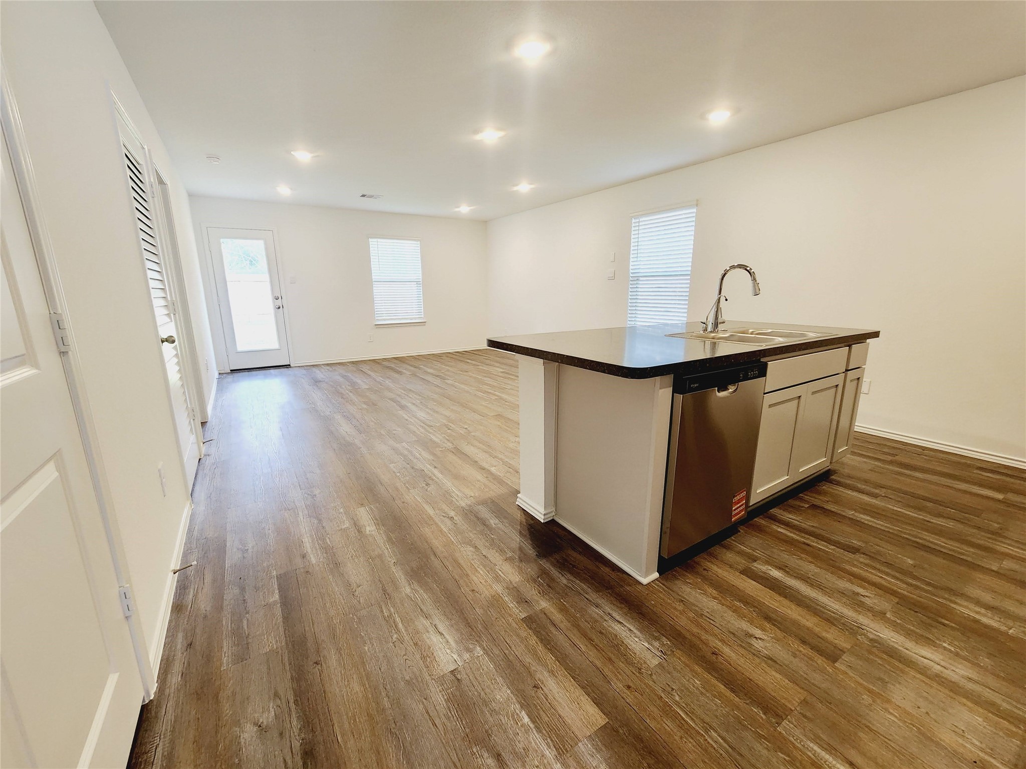 6043 Canyon Dawn Drive Spring, TX 77373 - Photo 7 of 31 a spacious, open-concept living area with wood-style flooring. The room features ample natural light, modern recessed lighting, and an island kitchen with stainless steel appliances and a sink, ideal for entertaining and daily living.