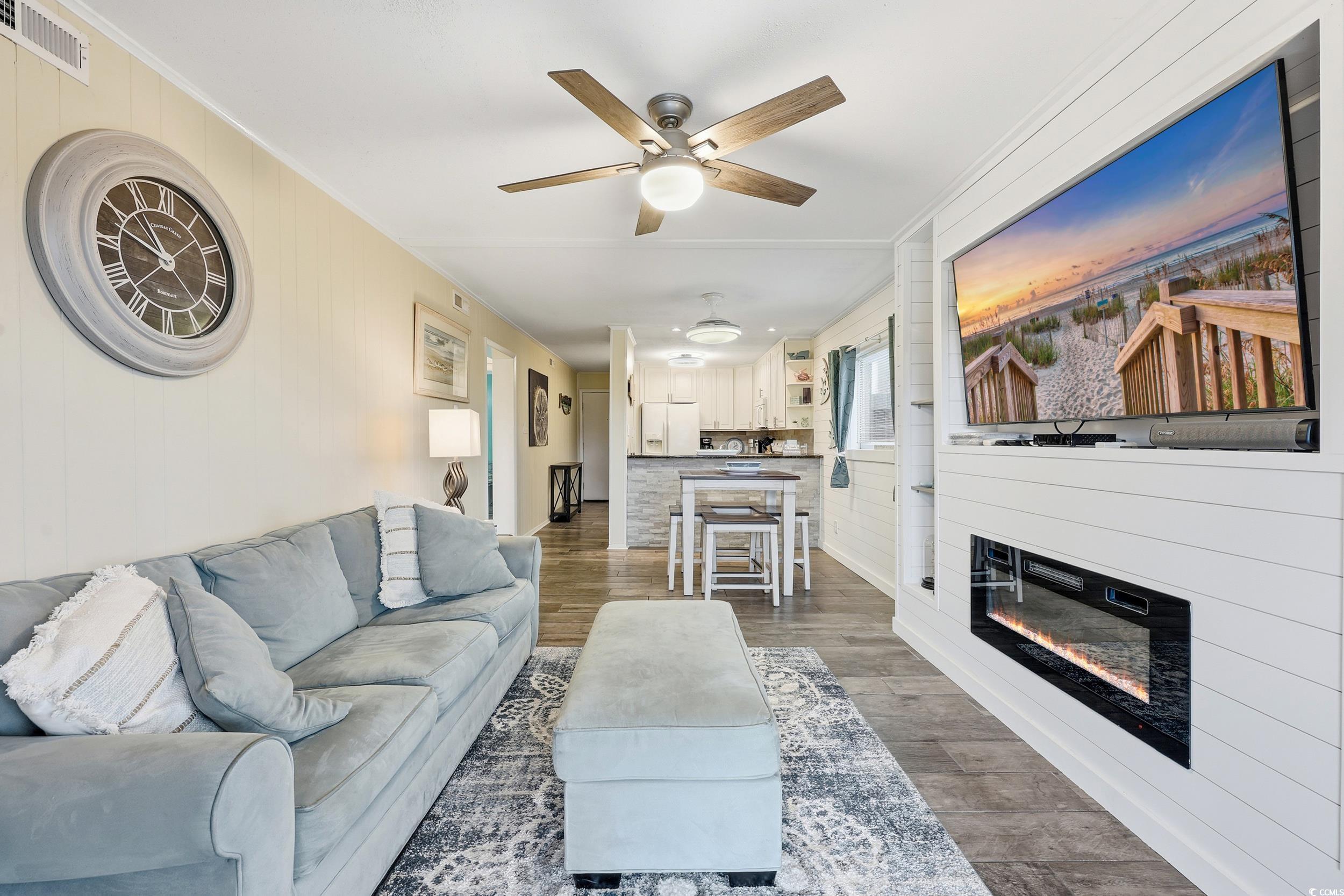 9501 Shore Drive, Unit A208 Myrtle Beach, SC 29572 - Photo 11 of 29 Living area with ornamental molding, wood walls, a glass covered fireplace, wood finished floors, and a ceiling fan