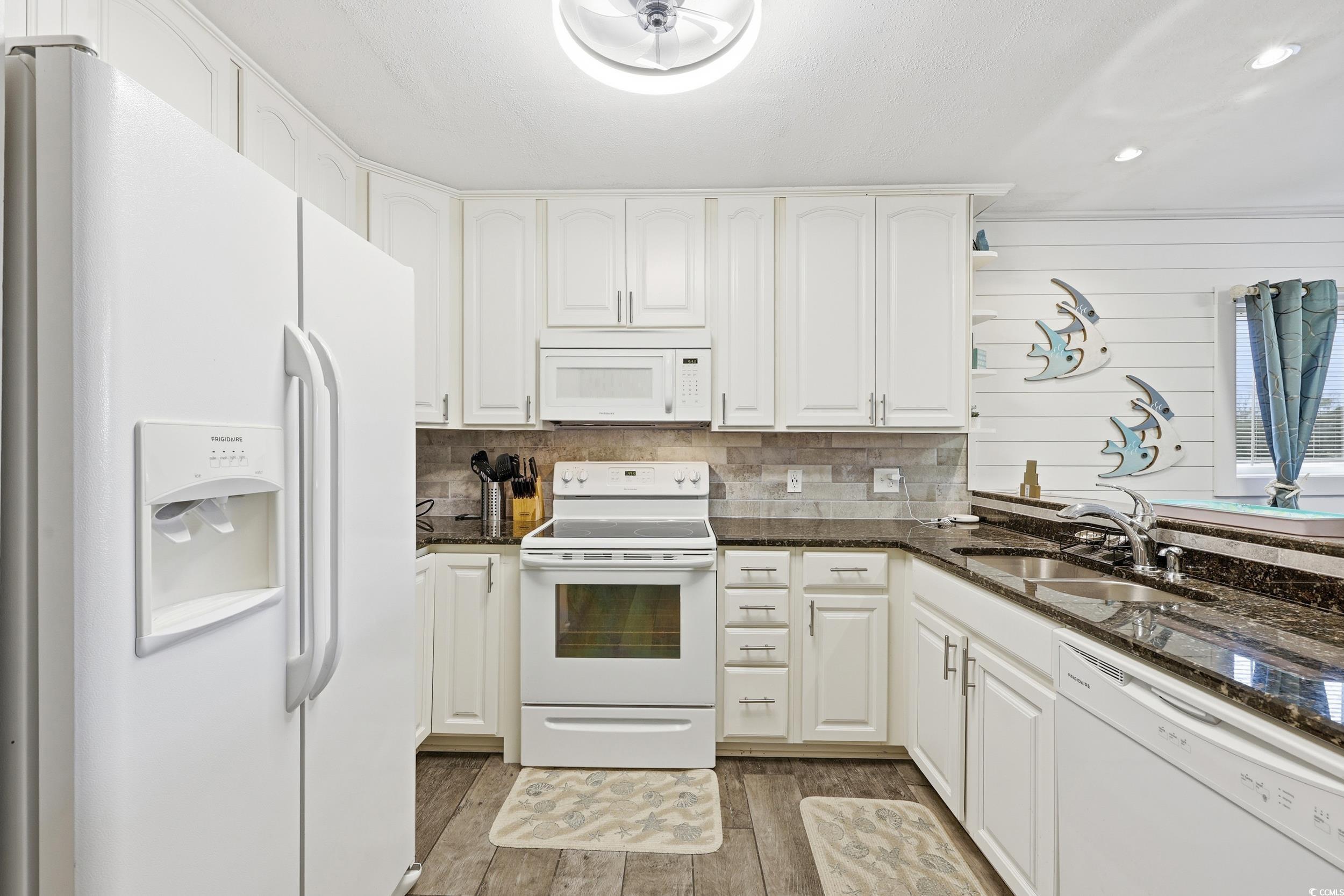 9501 Shore Drive, Unit A208 Myrtle Beach, SC 29572 - Photo 13 of 29 Kitchen with white appliances, dark stone countertops, white cabinetry, dark wood finished floors, and tasteful backsplash
