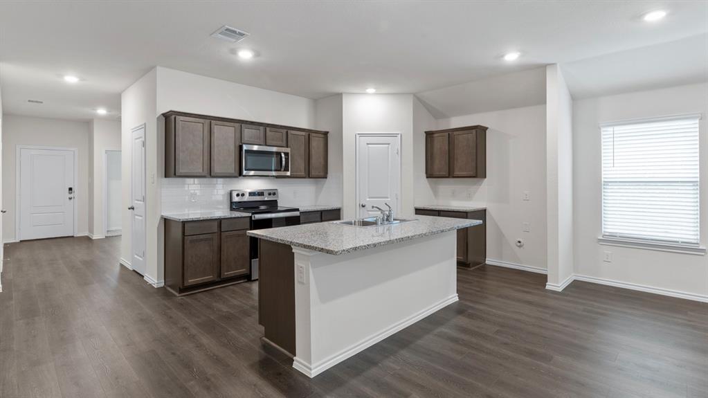 4028 Ripplewood Drive Lindale, TX 75771 - Photo 18 of 31 Kitchen featuring an island with a sink, stainless steel appliances, dark wood-finish cabinetry, and light-colored countertops