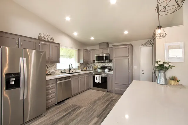 a kitchen with stainless steel appliances granite countertop a refrigerator a sink dishwasher a stove and white cabinets with wooden floor