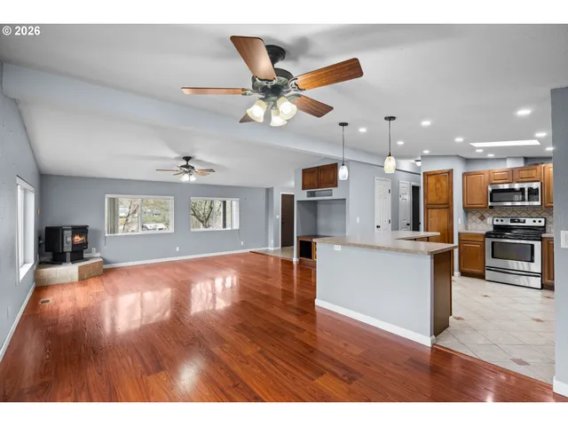 a view of an empty room and kitchen with wooden floor