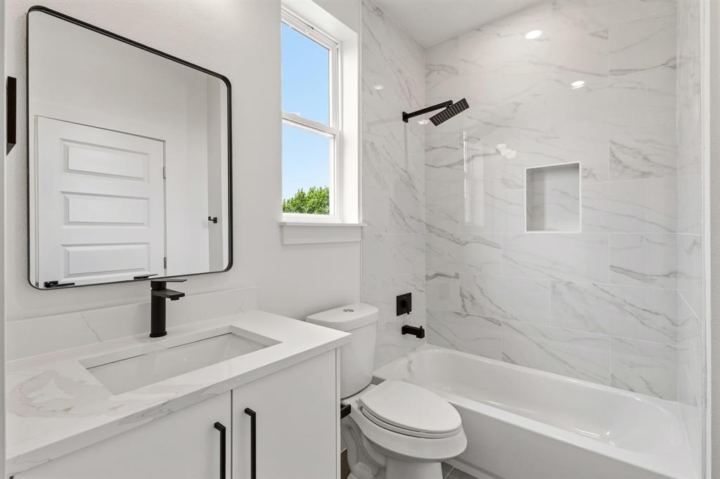 415 North Patton Avenue Dallas, TX 75203 - Photo 17 of 20 The bathroom features a vanity with a white countertop and black fixtures, a contemporary mirror, and a bathtub with white and gray tiled walls