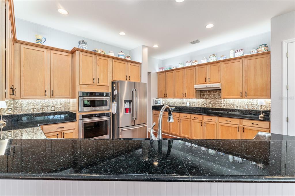 12895 Southeast 91st Terrace Road Summerfield, FL 34491 - Photo 27 of 99 a kitchen with stainless steel appliances granite countertop a refrigerator a stove and a sink with wooden cabinets