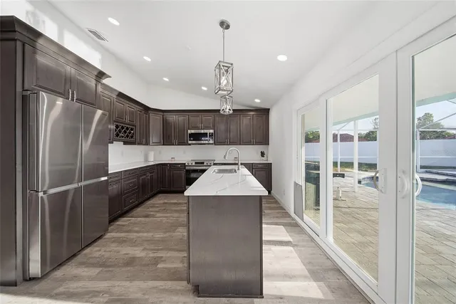 a large kitchen with kitchen island a large counter top a sink stainless steel appliances and cabinets