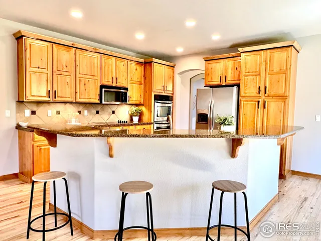 a kitchen with stainless steel appliances granite countertop a stove a refrigerator a microwave a dining table and chairs with wooden floor