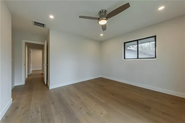 an empty room with wooden floor chandelier fan and windows