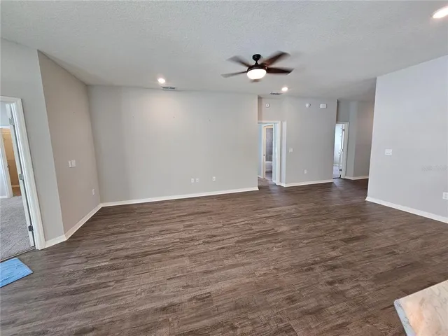 a view of an empty room with wooden floor and a ceiling fan