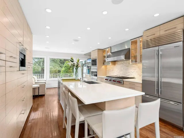 a white kitchen with a stove a sink a refrigerator and a dining table with wooden floor