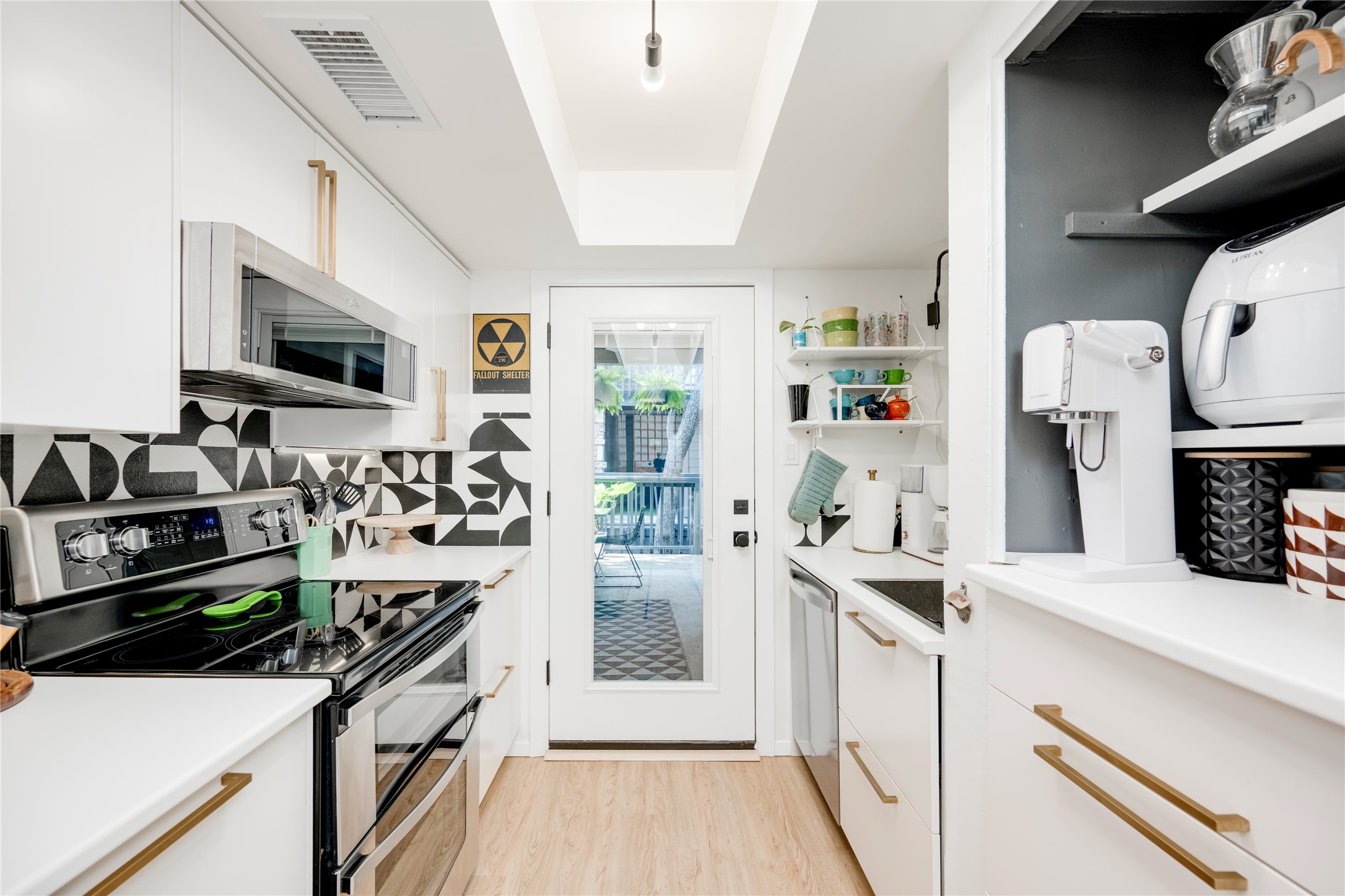 3627 Menchaca Road, Unit 214 Austin, TX 78704 - Photo 5 of 28 A well-lit kitchen with sleek white cabinetry and contrasting geometric backsplash, featuring a glass-paned door opening to a private deck.