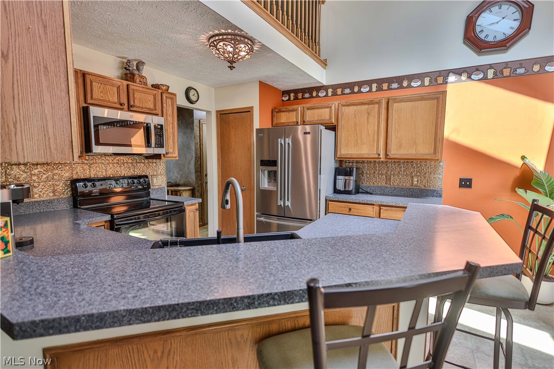 11154 Johnsford Road Southwest Beach City, OH 44608 - Photo 23 of 50 Kitchen featuring a breakfast bar with gray speckled countertops, stainless steel appliances, wood cabinetry, and a textured backsplash