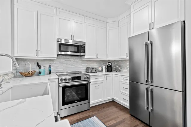 a kitchen with stainless steel appliances white cabinets white stove a refrigerator and a sink with wooden floor