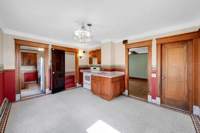 an empty room with chandelier and kitchen view