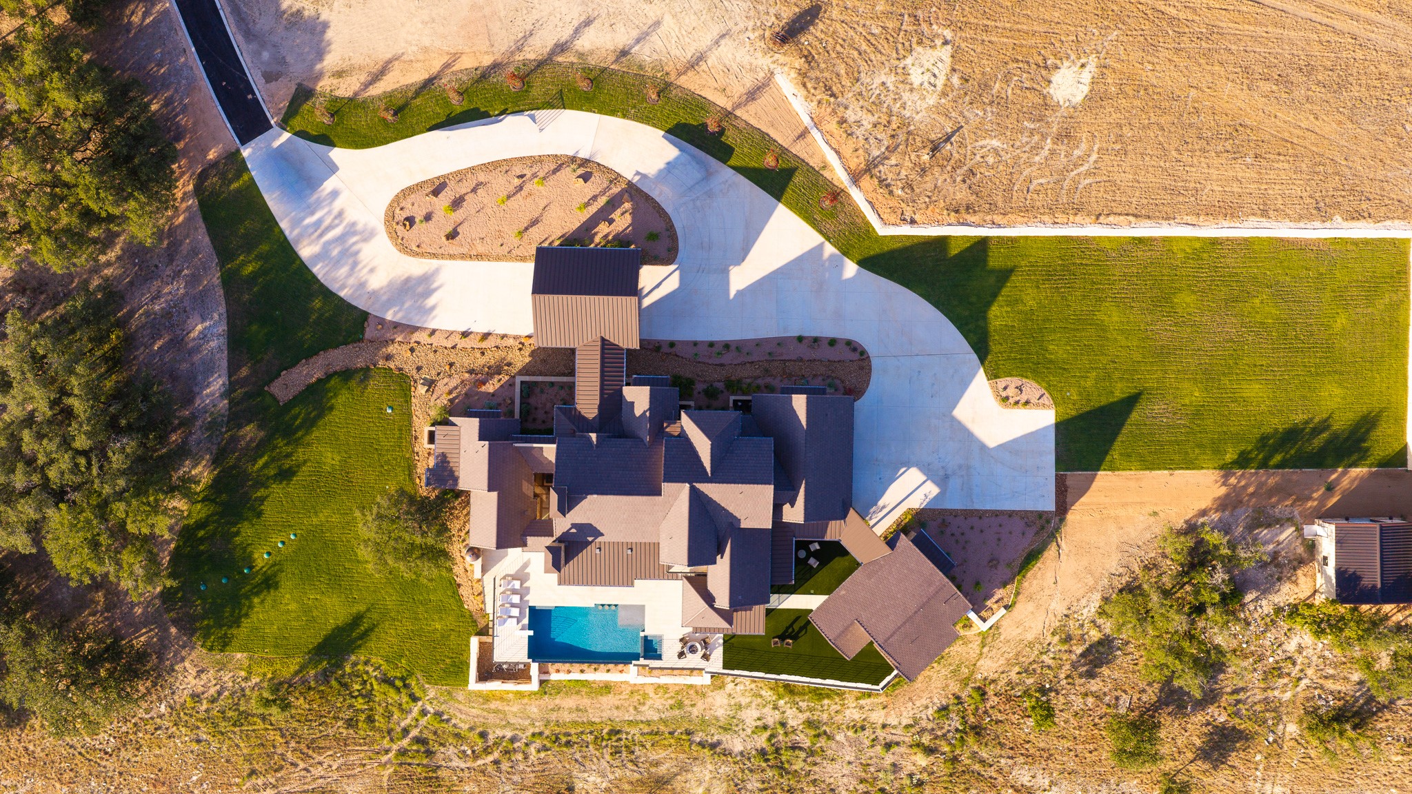 An aerial perspective showcases a sweeping circular driveway and an integrated backyard swimming pool.