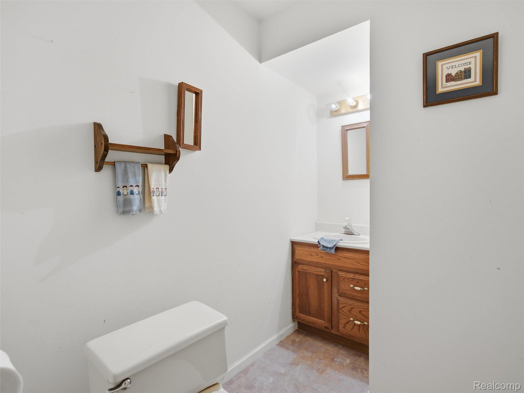 2195 London Bridge Drive Rochester, MI 48307 - Photo 11 of 30 White toilet, wood-finish vanity with a white countertop, and a wall-mounted mirror with integrated lighting