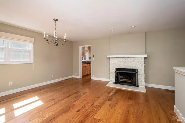 a view of an empty room with wooden floor fireplace and a window