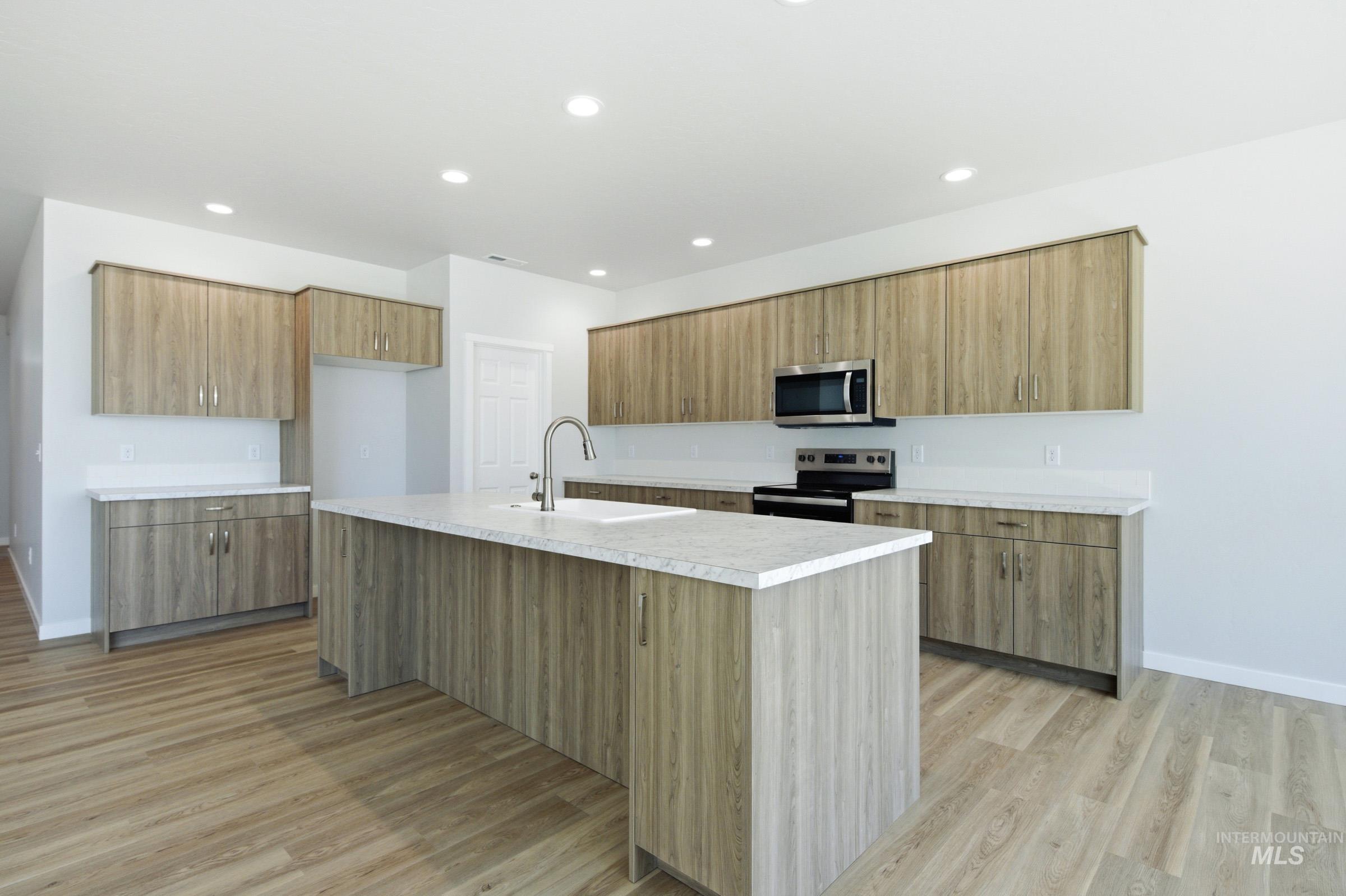 13649 Inman Court Caldwell, ID 83607 - Photo 5 of 22 Kitchen featuring a center island with integrated sink, stainless steel faucet, and light-toned countertops