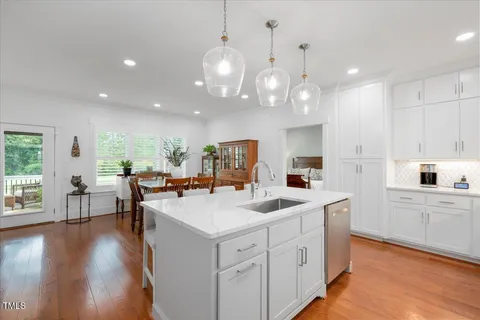 a kitchen with white cabinets a sink dishwasher and a dining table with wooden floor