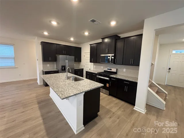 a large kitchen with stainless steel appliances a large counter top a stove a sink a refrigerator and a microwave