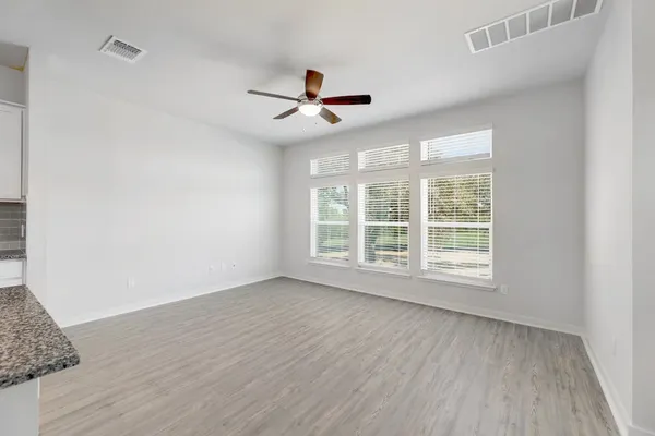 an empty room with wooden floor ceiling fan and windows