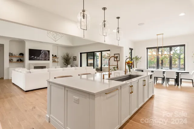 a large white kitchen with a stove a sink a dining table and chairs with wooden floor
