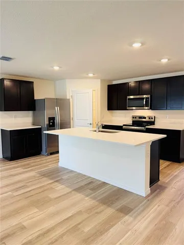 a large kitchen with kitchen island a counter top a sink stainless steel appliances and cabinets