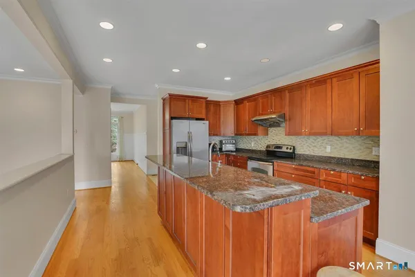 a kitchen with stainless steel appliances granite countertop a sink a stove top oven a refrigerator and dishwasher with wooden floor