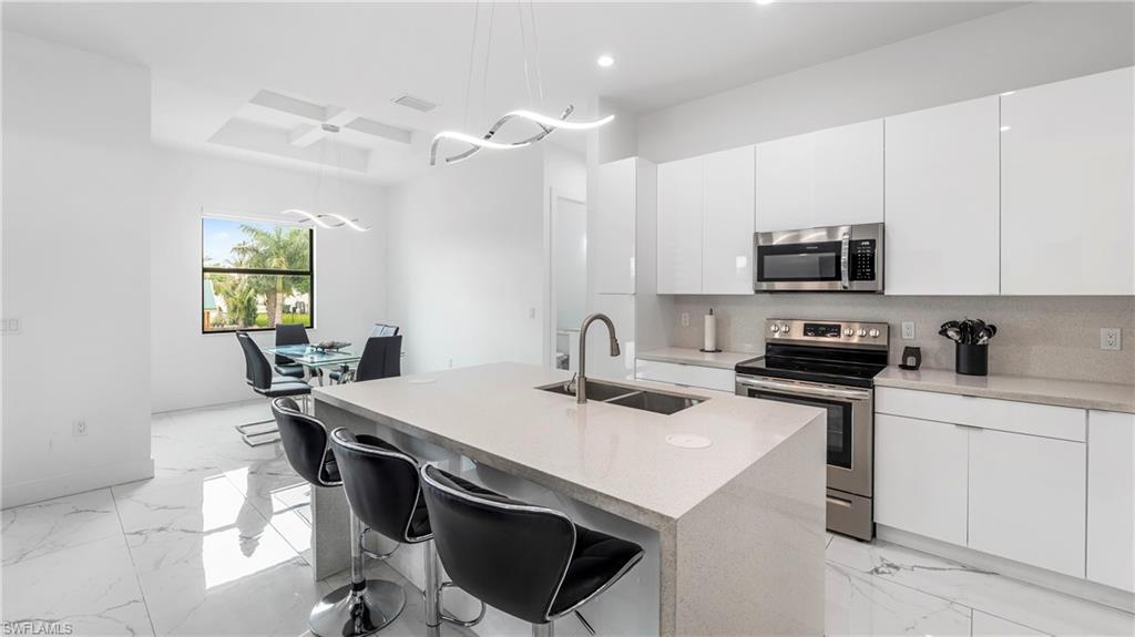 2998 52nd Street Southwest Naples, FL 34116 - Photo 11 of 44 Kitchen featuring stainless steel appliances, a kitchen bar, white cabinets, and modern cabinets