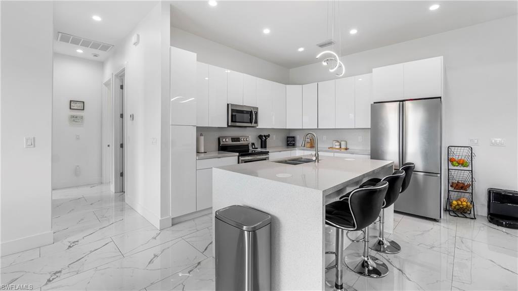 2998 52nd Street Southwest Naples, FL 34116 - Photo 12 of 44 Kitchen featuring stainless steel appliances, modern cabinets, a center island with sink, and white cabinetry