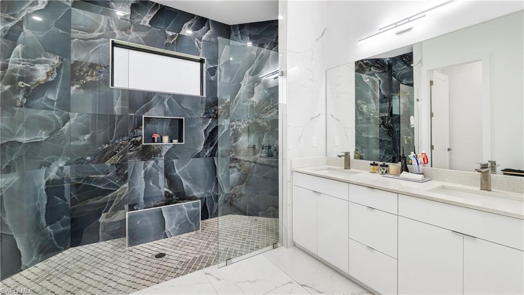 2998 52nd Street Southwest Naples, FL 34116 - Photo 22 of 44 Bathroom featuring double vanity, a marble finish shower, stone wall, and light marble finish flooring