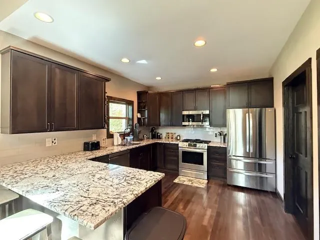 a kitchen with stainless steel appliances granite countertop a refrigerator oven a sink dishwasher and wooden cabinets with wooden floor