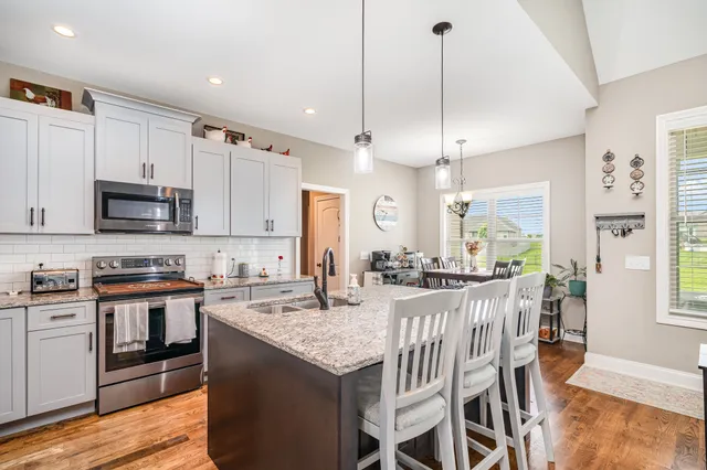 a kitchen with stainless steel appliances granite countertop a stove top oven a sink dishwasher a dining table and chairs with wooden floor