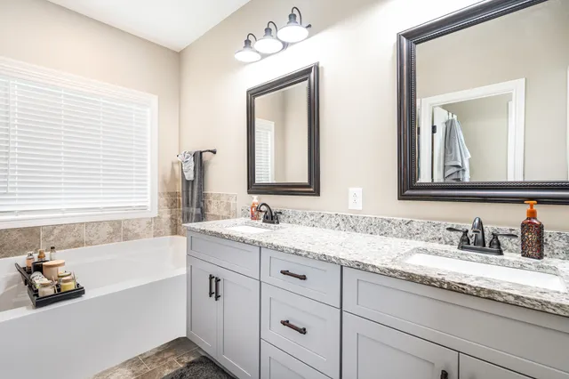 a bathroom with double vanity sinks a large mirror a bathtub and next to a window