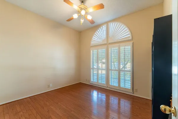 an empty room with wooden floor fan and windows