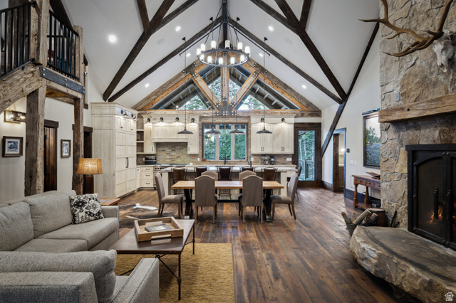 1667 West Tollgate Cyn Road Coalville, UT 84017 - Photo 7 of 61 Open-concept living space featuring vaulted ceilings with exposed wood beams, wood-finish flooring, a stone fireplace with a substantial hearth, and a kitchen with light wood cabinetry and pendant lighting