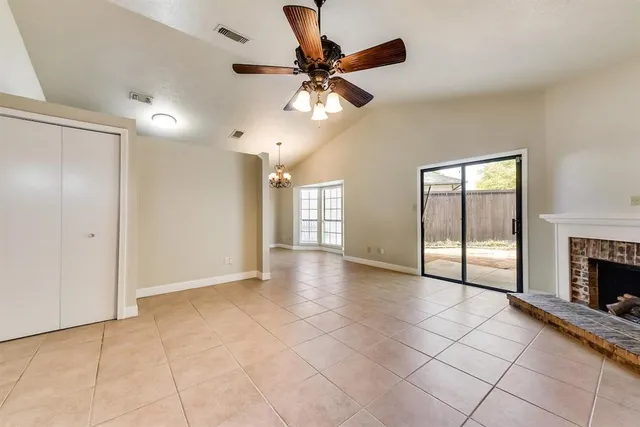 a view of an empty room with chandelier fan and fire place
